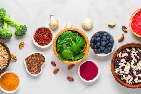 Verschiedene Superfoods wie Spinat, Blaubeeren, Brokkoli und Bohnen auf weißem Tisch