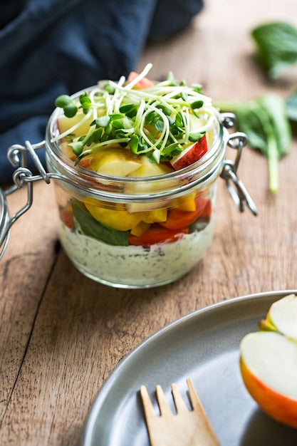 Schichtsalat im Einmachglas mit Gemüse, Kräuterdip und Sprossen auf Holztisch