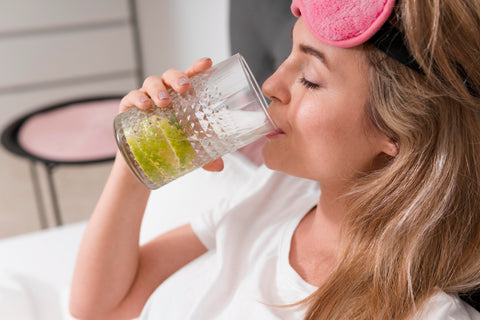 Frau mit rosa Schlafmaske trinkt Limettenwasser im Bett, Gesundheit und Entspannung
