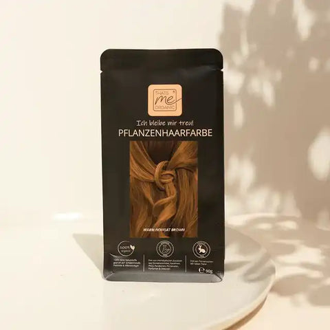 That's Me Organic Pflanzenhaarfarbe Warm Nougat Brown auf weißem Teller, beige Hintergrund
