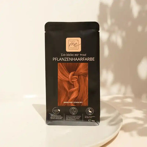 Bio Pflanzenhaarfarbe Verpackung, warmes Henna Rot, auf hellem Teller vor neutralem Hintergrund.