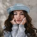 Frau mit langen braunen Haaren und hellblauem Hut trägt grauen Strickpullover, Nahaufnahme