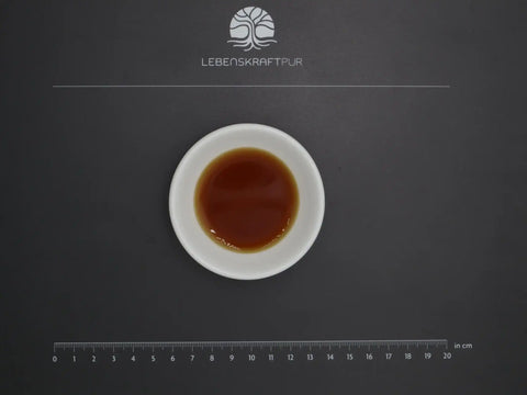 Weiße Schale mit braunen Bio Bitterkräuter Tropfen auf schwarzer Unterlage, Maßstab und LebensKraftPur-Logo