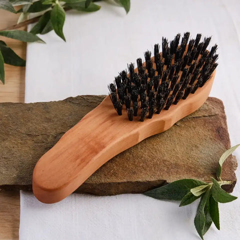 Holzbürste mit dunklen Borsten auf Steinplatte, Naturdeko und weißem Hintergrund