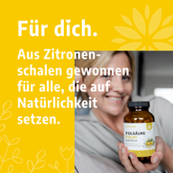 Frau hält Glas mit VitaLove Folsäure aus Zitronenschalen auf gelbem Hintergrund mit Text.