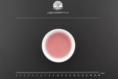 Weiße Schale mit rosa Gold-Kolloid-Lösung auf schwarzer Unterlage, Maßstab und Logo