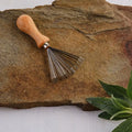 Mini-Gartenrechen mit Holzgriff auf Naturstein, Gartengerät, Kräuterpflanze am Rand