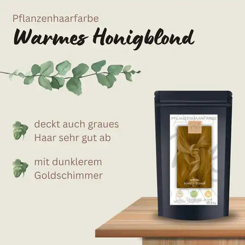 Pflanzenhaarfarbe warmes Honigblond Packung auf Holztisch mit Produktbeschreibung und Blättern.