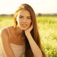 Junge Frau mit langen braunen Haaren im Sommerkleid auf blühendem Feld bei Sonnenlicht