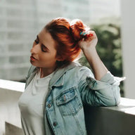 Junge Frau mit roten Haaren, Jeansjacke und weißem T-Shirt draußen auf Balkon