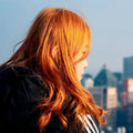 Frau mit leuchtend rot-orangen Haaren im Sonnenlicht vor einer Stadt-Skyline