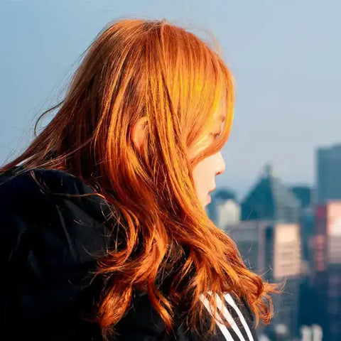 Frau mit leuchtend rot-orangen Haaren im Sonnenlicht vor einer Stadt-Skyline