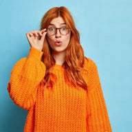Frau mit roten Haaren und Brille im orangefarbenen Strickpullover vor blauem Hintergrund