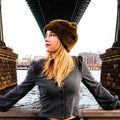 Frau mit brauner Fellmütze und grauer Bluse unter Brücke in urbaner Stadtlandschaft