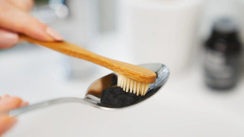 Bambuszahnbürste mit Zahnpulver auf Löffel, vegane Zahnpflege im Badezimmer