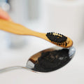Holzzahnbürste mit schwarzem Zahnpulver und Löffel, natürliche Mundpflege Nahaufnahme