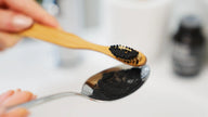 Holzzahnbürste mit schwarzem Zahnpulver und Löffel, natürliche Mundpflege Nahaufnahme