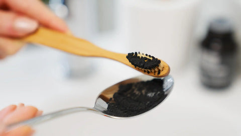 Holzzahnbürste mit schwarzem Zahnpulver und Löffel, natürliche Mundpflege Nahaufnahme