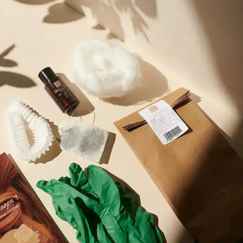 Friseurbedarf Set mit grünem Handschuh, Flasche, Teebeutel, Haarband, Watte und Papiertüte auf Tisch